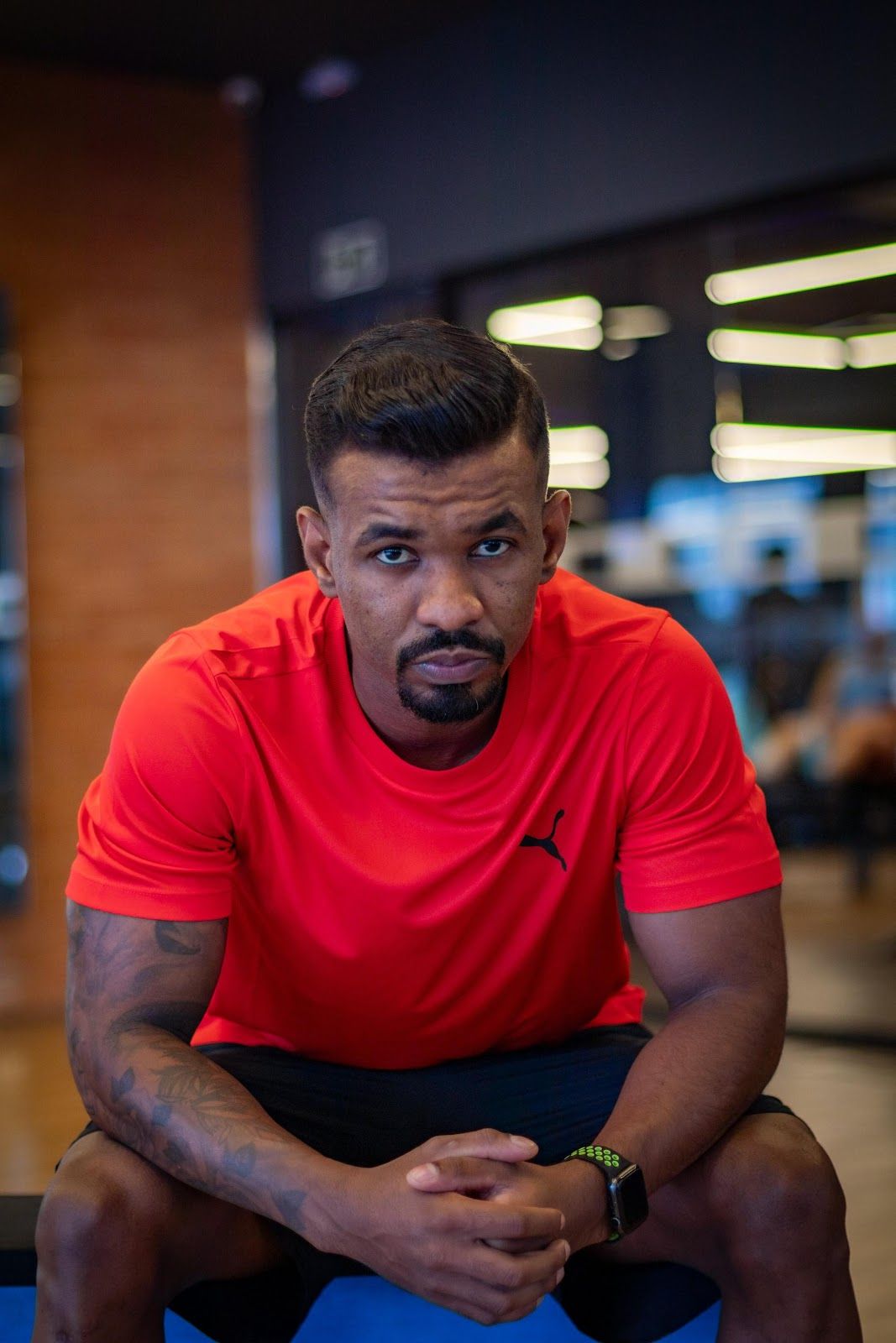 Lucas sentado na academia, de camiseta vermelha